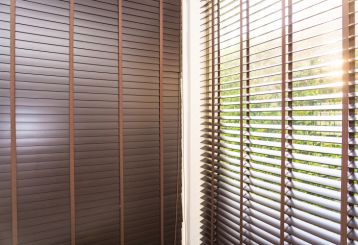 Faux wood blinds in a beautiful wooden finish, gracing a living room window with soft, filtered sunlight.